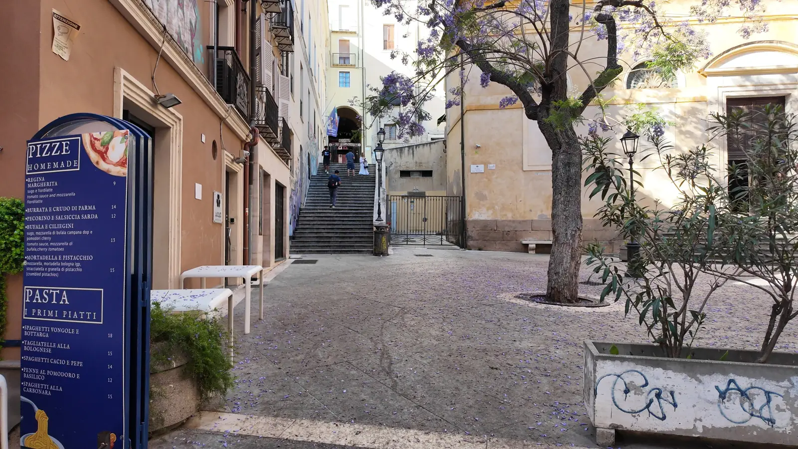 A sunny piazza in the old town of Cagliari with jacaranda trees and steps climbing up