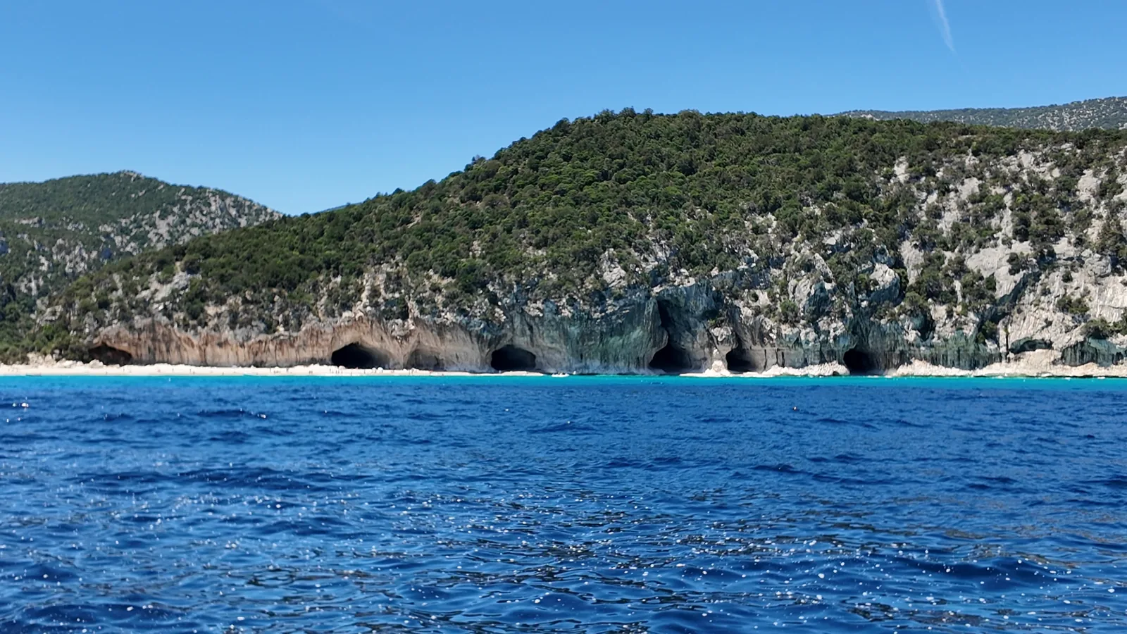 The cliffs and sea caves at Cala Luna from a boat on deep blue water