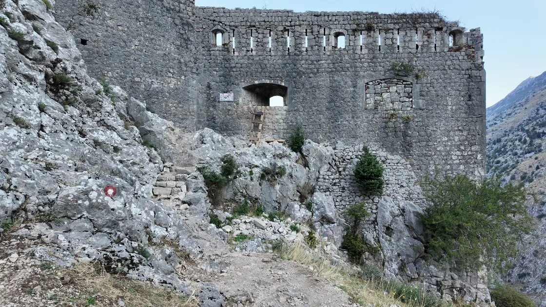 A ruined stone fortress wall with an arched window on bare rock above Kotor