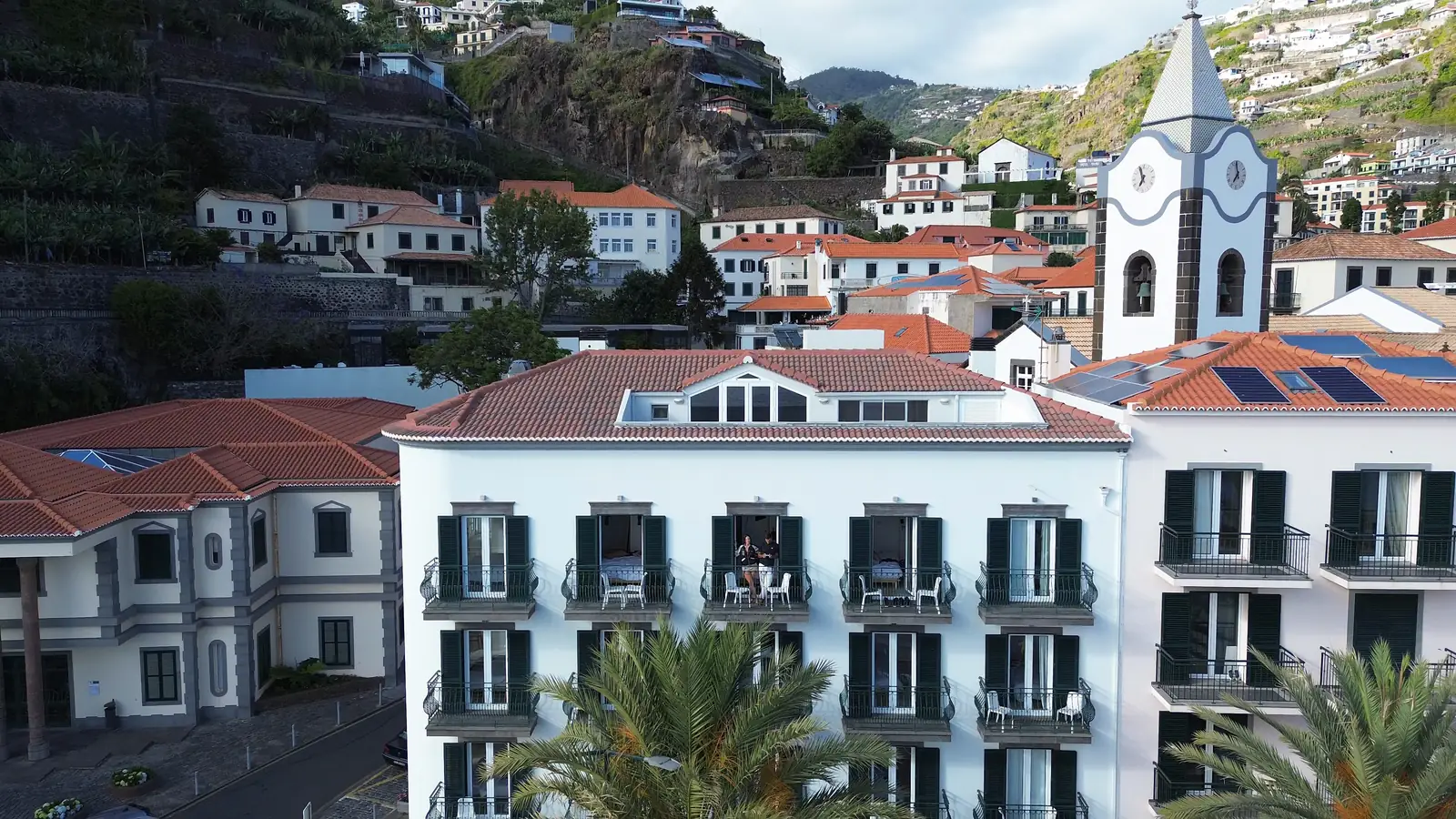 The white hotel front and church tower of Ponta do Sol, with houses stacked up the green hillside