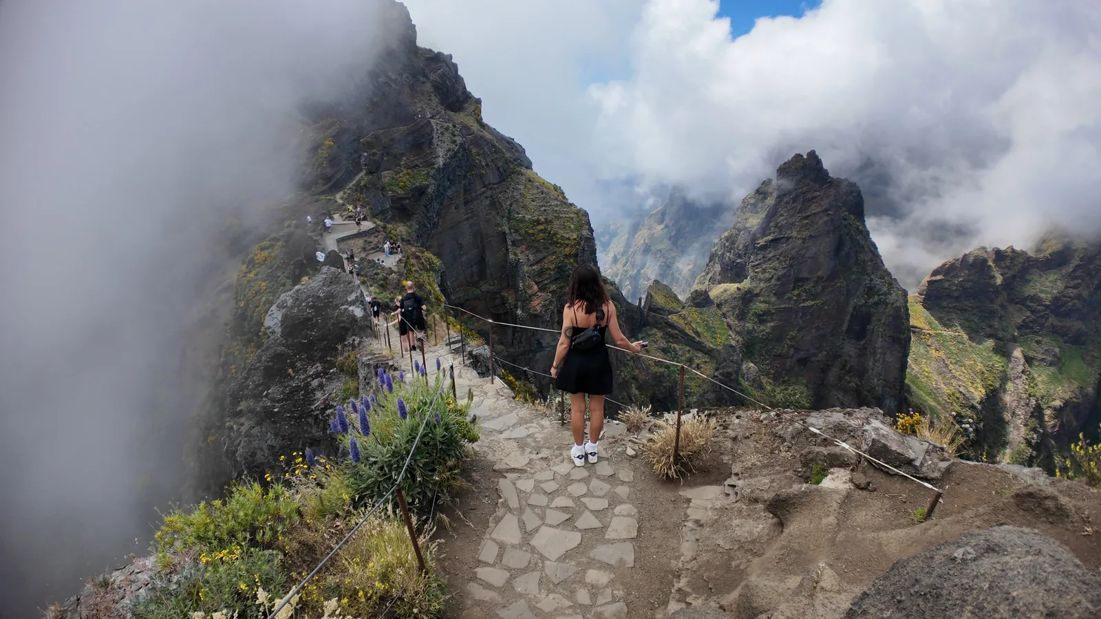 Abbey walking the paved PR1 ridge path between the jagged peaks, with cloud pouring over the mountains